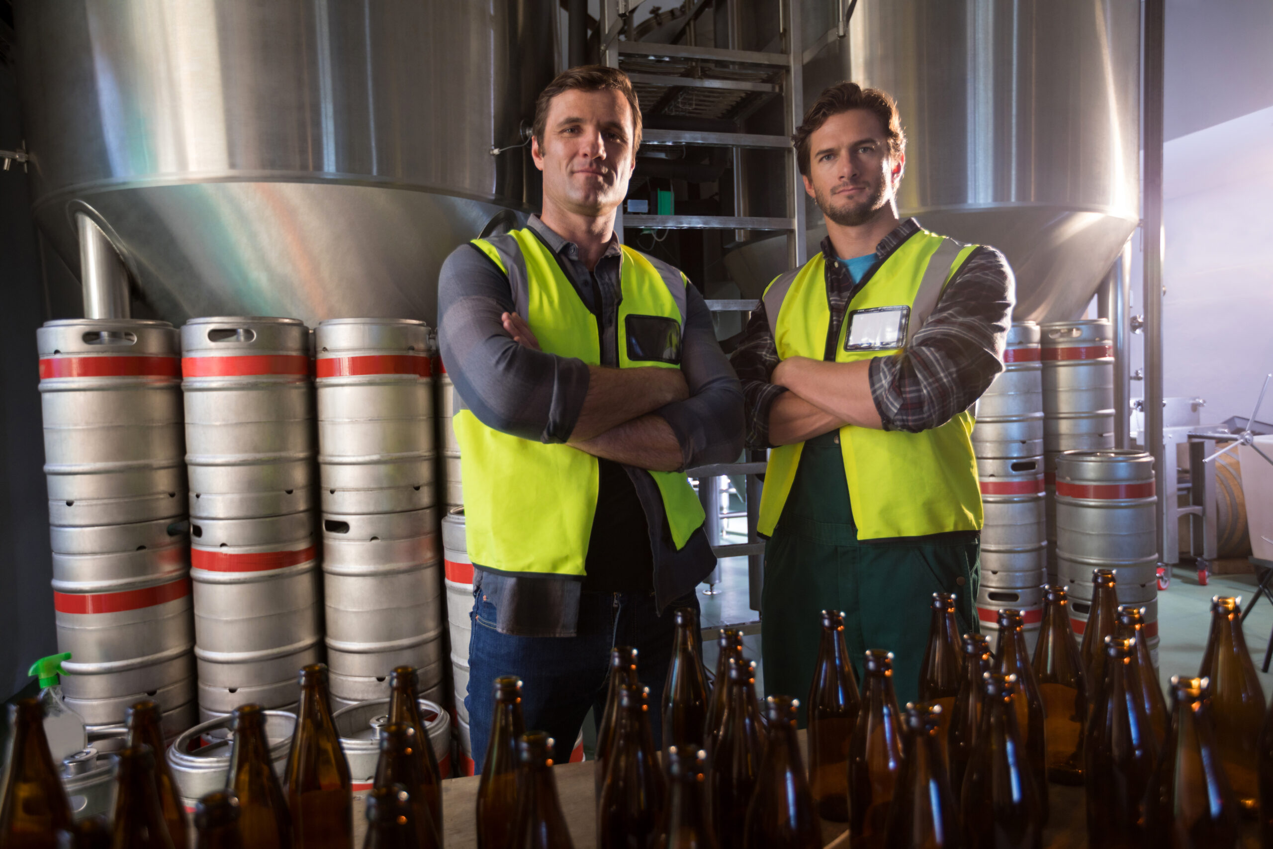 Portrait of coworkers with arms crossed standing by beer bottles
